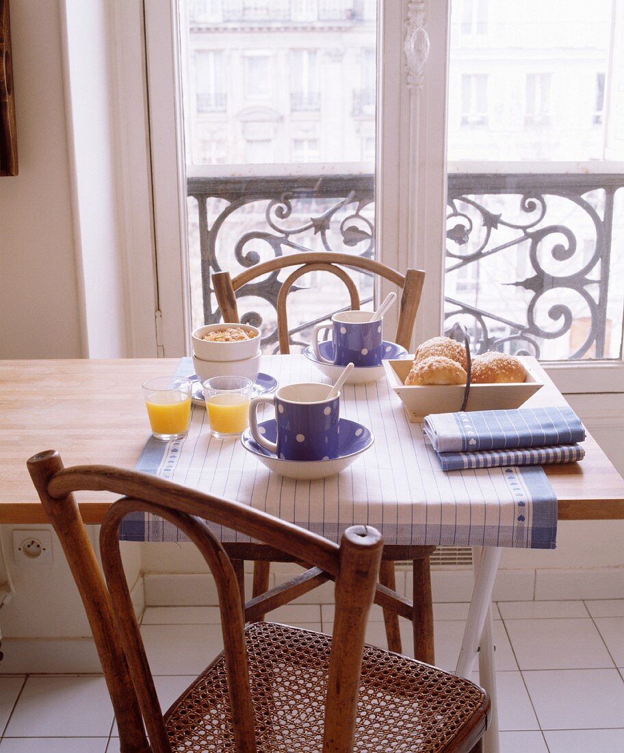 Antike Holzstühle mit Sitzgeflecht an modernem, blauweiss gedecktem Frühstückstisch vor französischem Altbau-Fenster