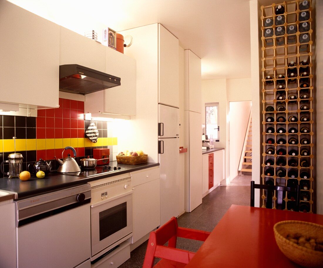 Raumhohes Weinflaschenregal in Wandnische neben rotem Tisch in moderner, weisser Küche