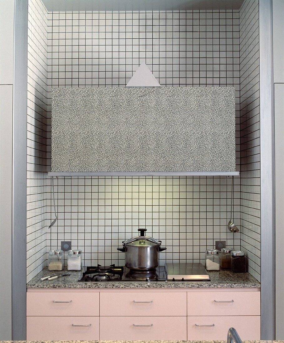 Küchennische mit rosefarbenen Fronten und Kochfeld in Granitarbeitsplatte unter kastenförmigem Dunstabzug