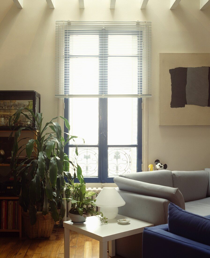 Graues und blaues Sofa korrespondiert mit abstrakter Malerei und Jalousie vor blauem französischen Fenster in modernem Wohnzimmer