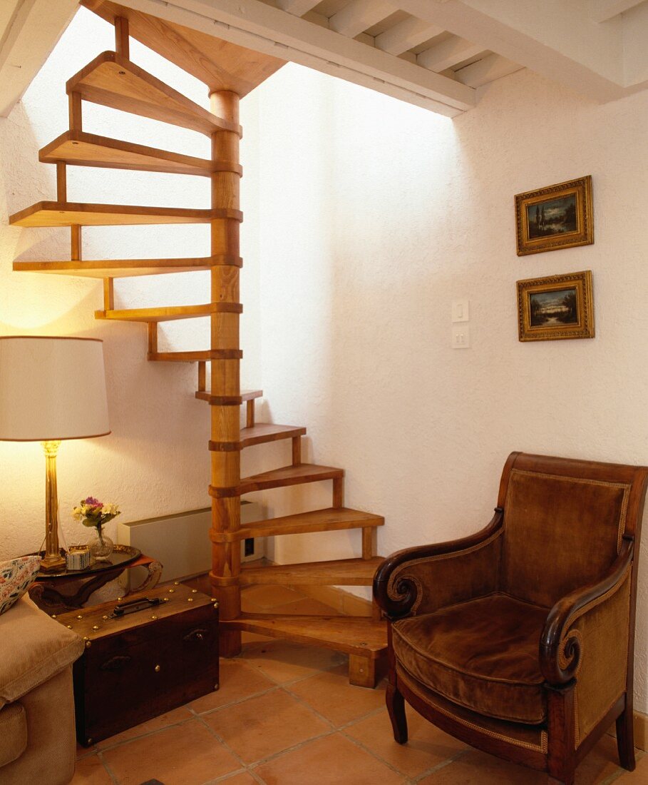 Antiker Plüschsessel unter hölzerner Wendeltreppe und weisser Holzbalkendecke in Landhaus-Wohnzimmer