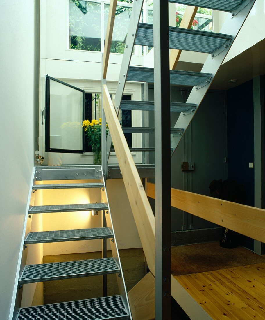 Geöffnetes Fenster hinter moderner Stahltreppe mit Gitterroststufen und Holzbrett als Geländer