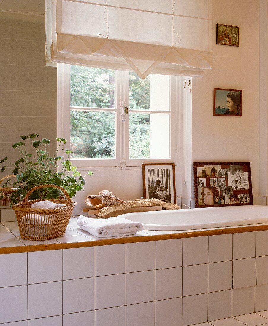 Fotos und grosse Muschel vor Sprossenfenster mit Faltrollo über eingebauter Wanne in weiss gefliestem Bad