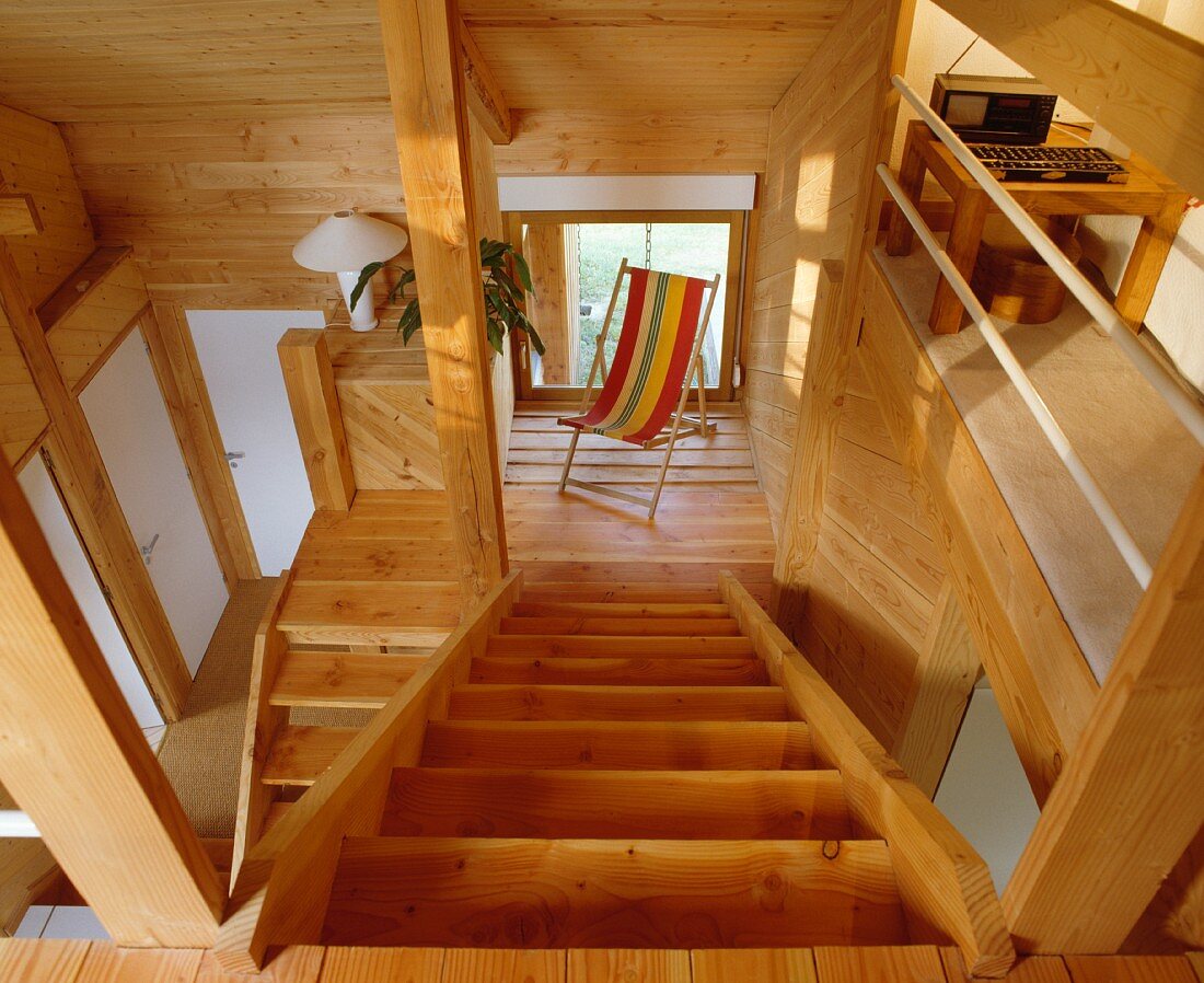Blick auf Treppenpodest mit gestreiftem Liegestuhl in offenem, holzverkleidetem Wohnraum