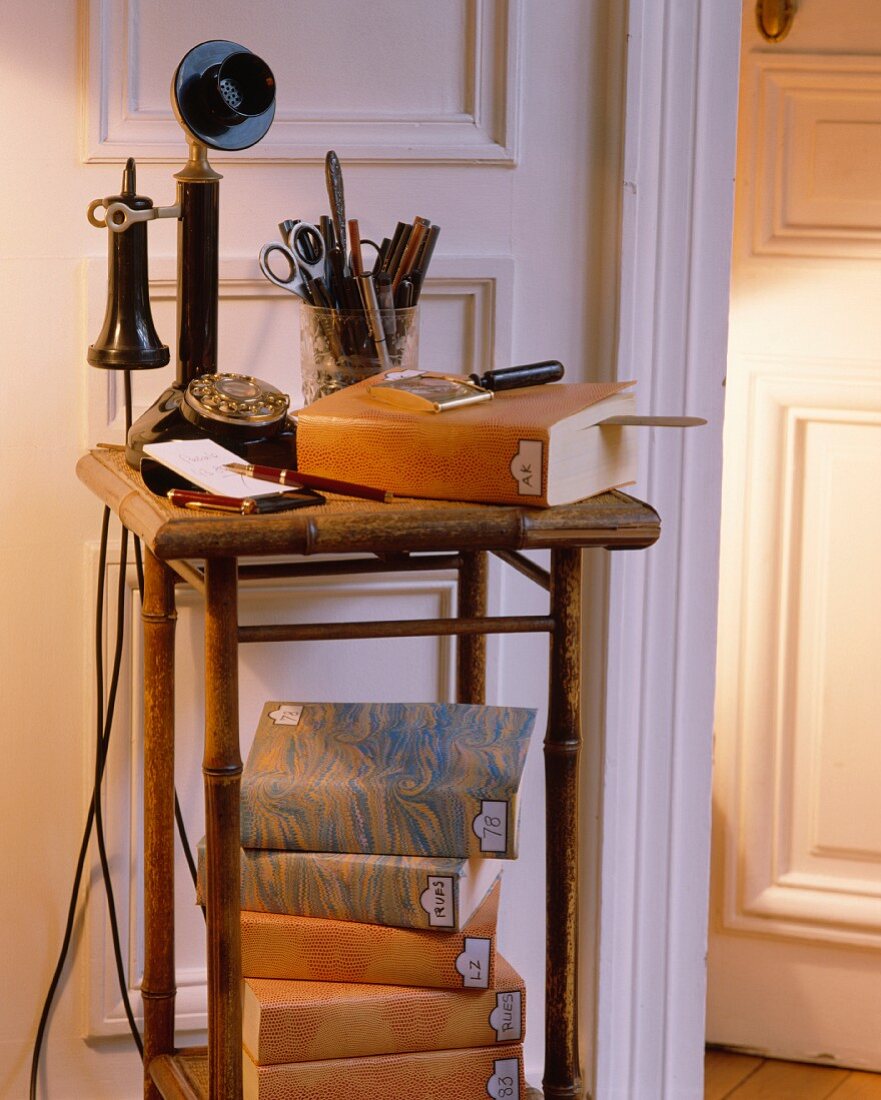 30er-Jahre-Telefon und Stapel Bücher mit marmoriertem Einband auf altem Bambustisch