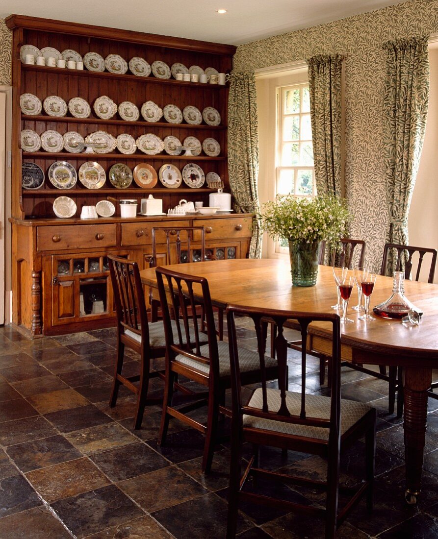 Grosse, antike Anrichte mit Tellersammlung in Landhaus-Esszimmer mit floral gemusterten Tapeten und passenden Vorhängen