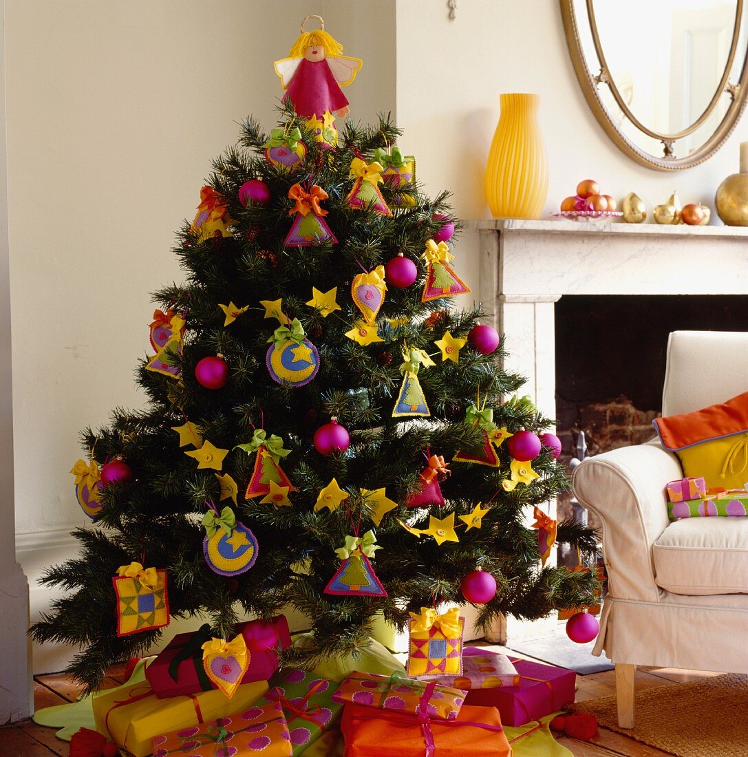 Poppiger Weihnachtsbaum und Geschenkpäckchen in Pink, Gelb und Orange neben Polstersessel und traditionellem Kamin