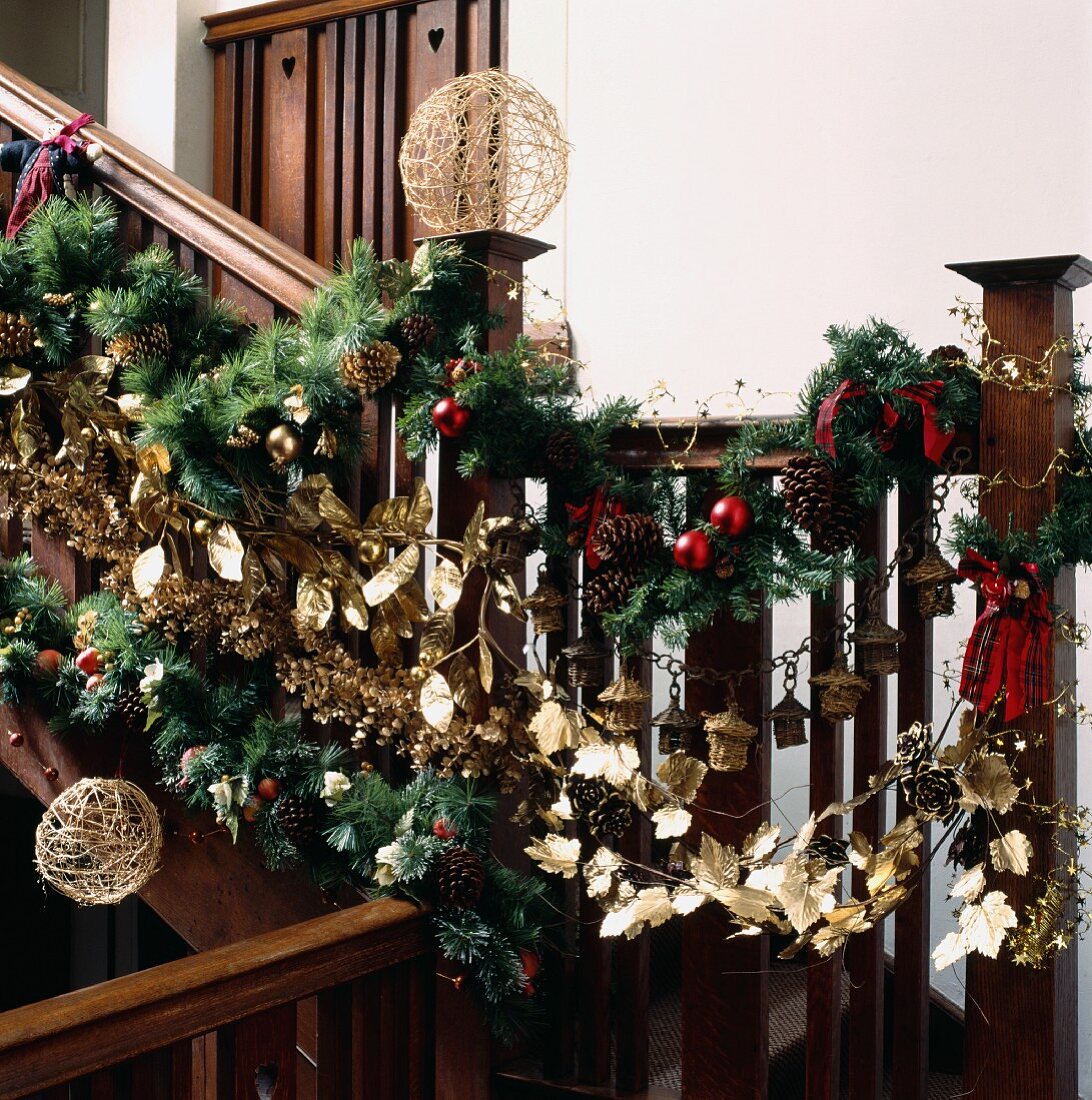 Üppige, englische Weihnachtsgirlande aus Tannenzweigen, Goldblättern und roten Kugeln an hölzernem Treppengeländer
