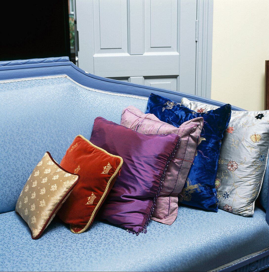 Verschiedene Kissen in Blau-/Lilatönen aus Seide und Samt auf blauem Sofa