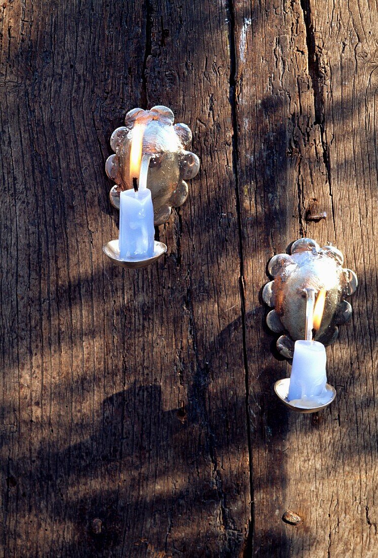 Silberner Wandkerzenhalter mit brennenden Kerzen auf rohem Holz