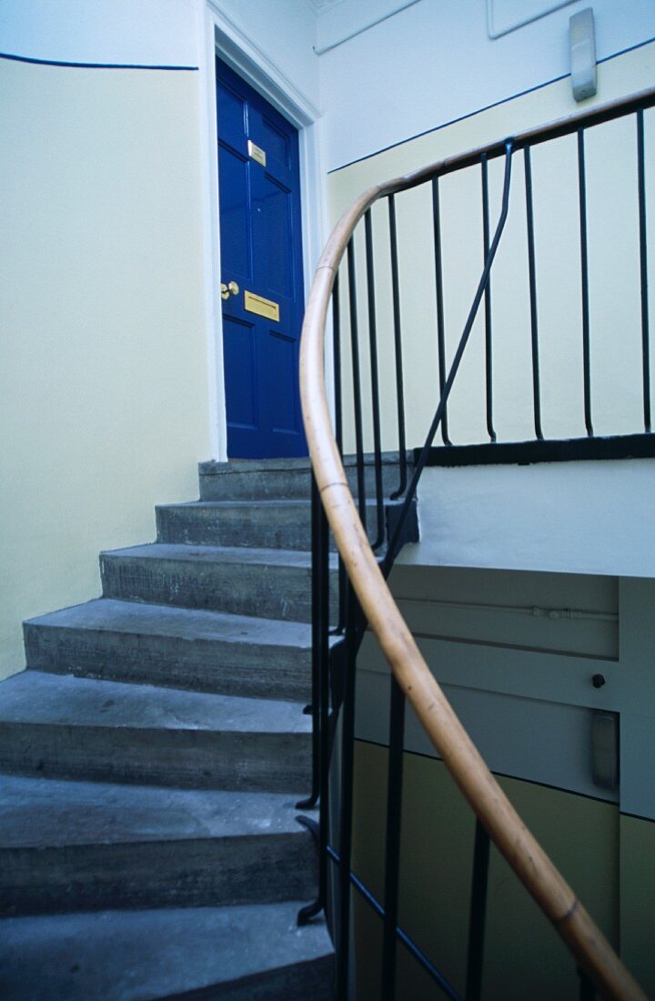 Treppenaufgang aus Beton mit modernem Geländer und Blick auf blaue traditionelle Wohnungstür