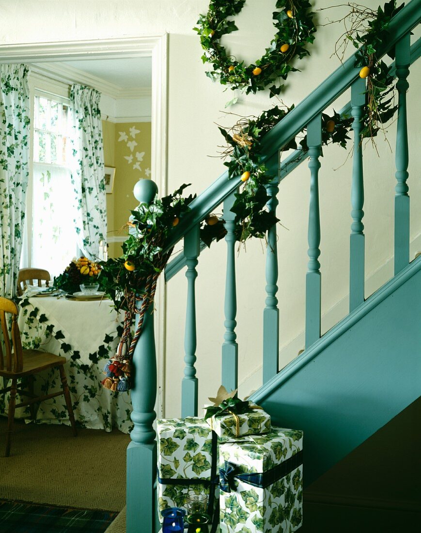 Türkisblaues, traditionelles Treppengeländer mit weihnachtlicher Efeugirlande und Geschenken neben Blick in Esszimmer