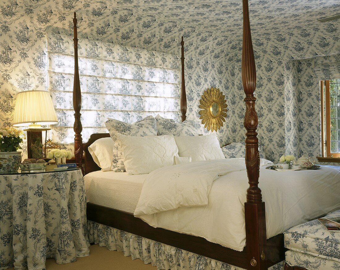 Ein Doppelbett mit gedrechseltem Gestell aus Mahagoni in Schlafzimmer mit blau-weisser Tapete und passenden Stoffen