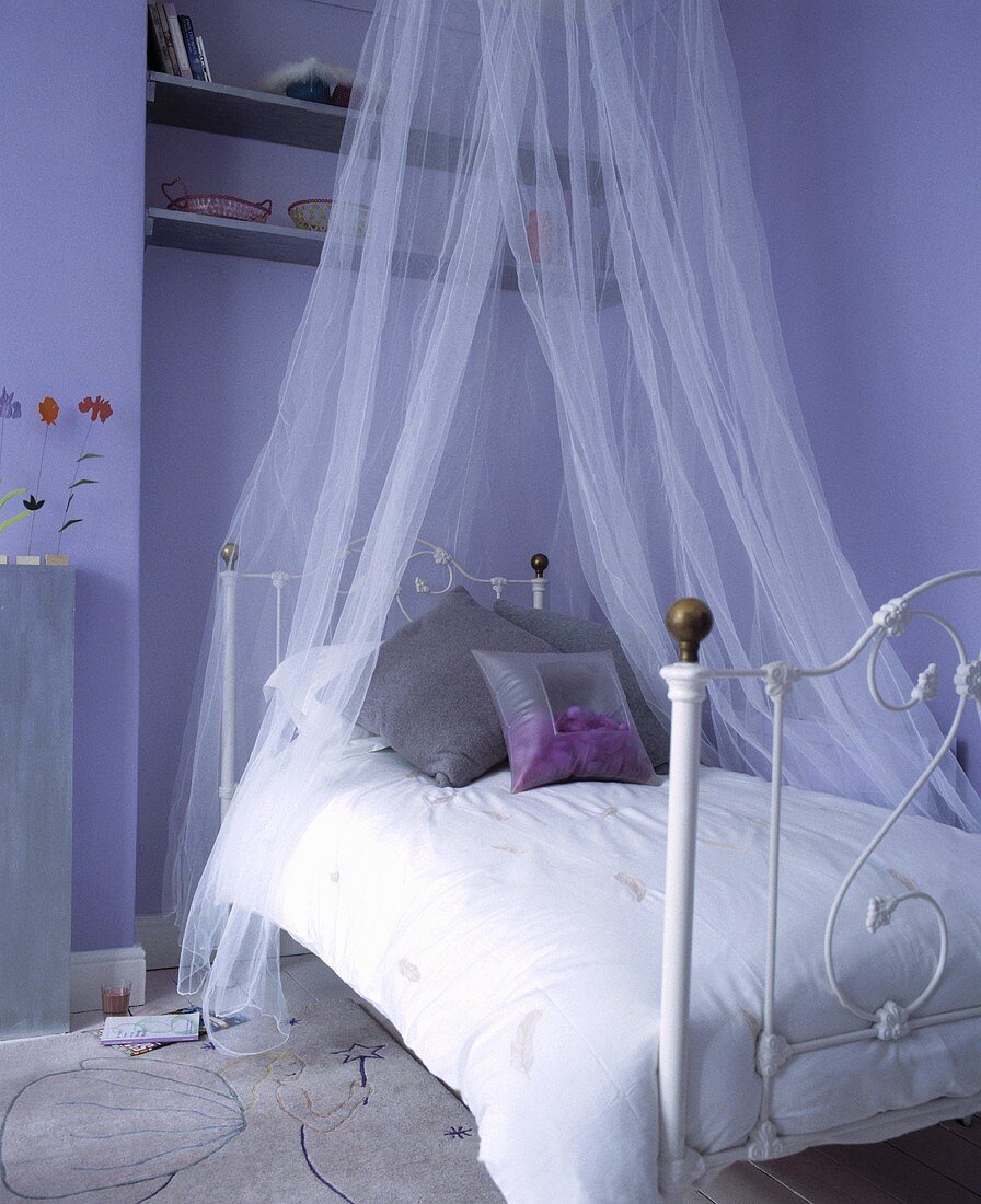 Ein weisses schmiedeeisernes Bett mit Baldachin und weisser Bettwäsche in einem lila Schlafzimmer