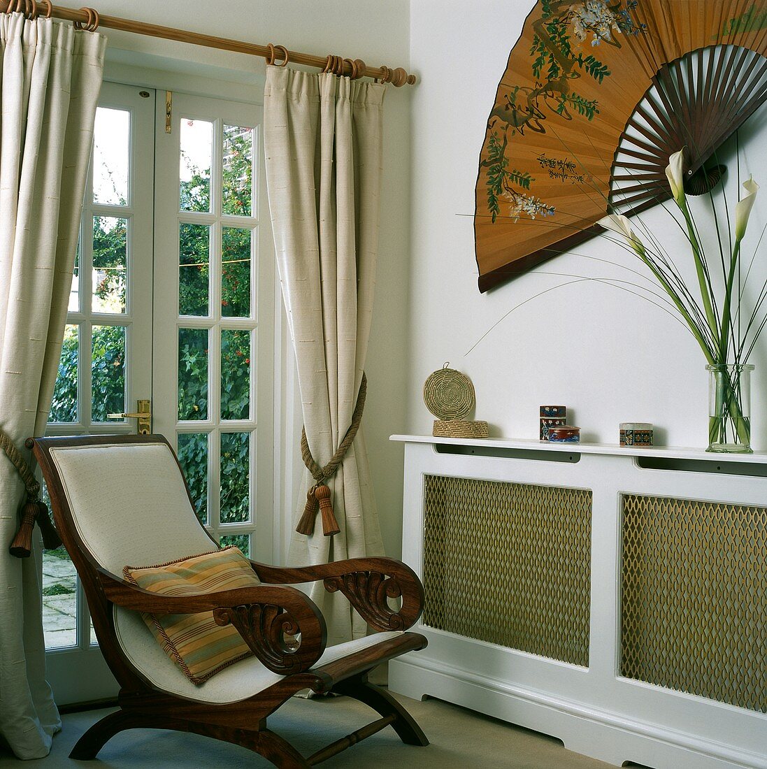Armlehnstuhl (Planter's Chair) im Landhausstil vor Terrassentür und Wanddekoration mit großem Fächer über verkleidetem Heizkörper