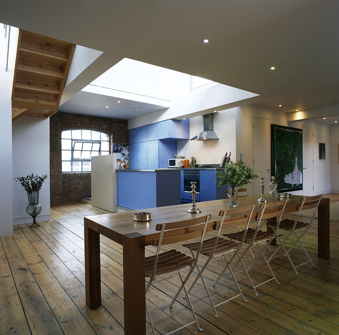 Langer Esstisch mit Stühlen und eine blaue Küche in einer Loftwohnung