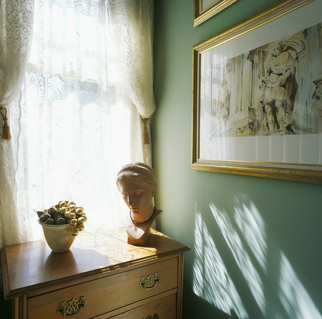 Eine Büste auf einer Kommode aus Kiefer vor dem Fenster in einem Zimmer mit türkisfarbener Wand