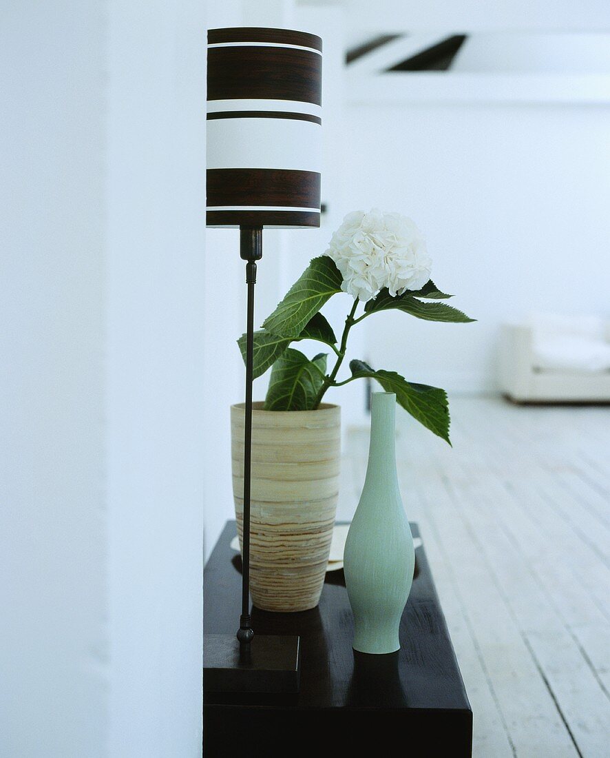 Eine Tischlampe mit schwarz-weißem Schirm neben einer Vase mit Hortensie