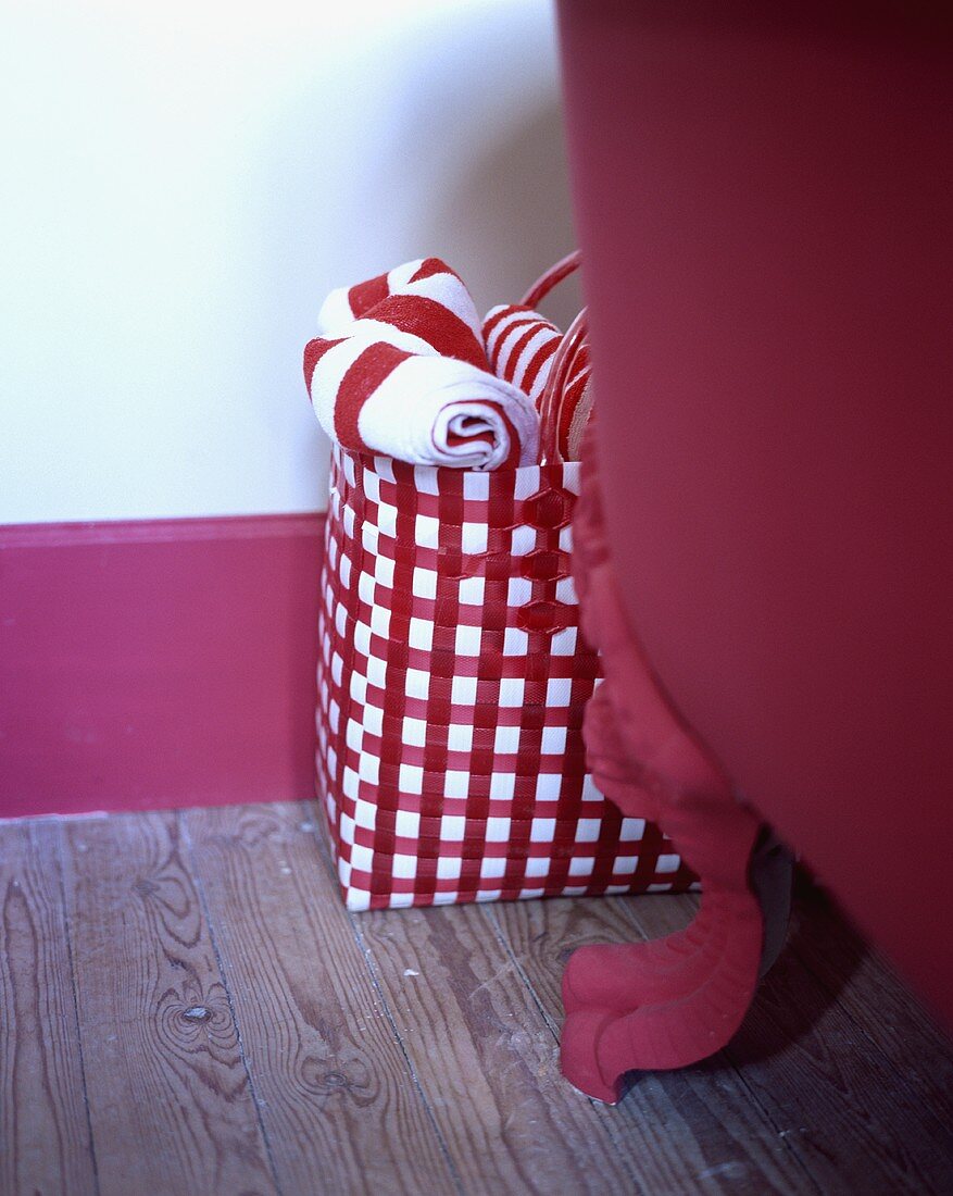 Rot-weiss karierte Tasche mit rot-weissen Handtüchern neben einer frei stehenden roten Badewanne