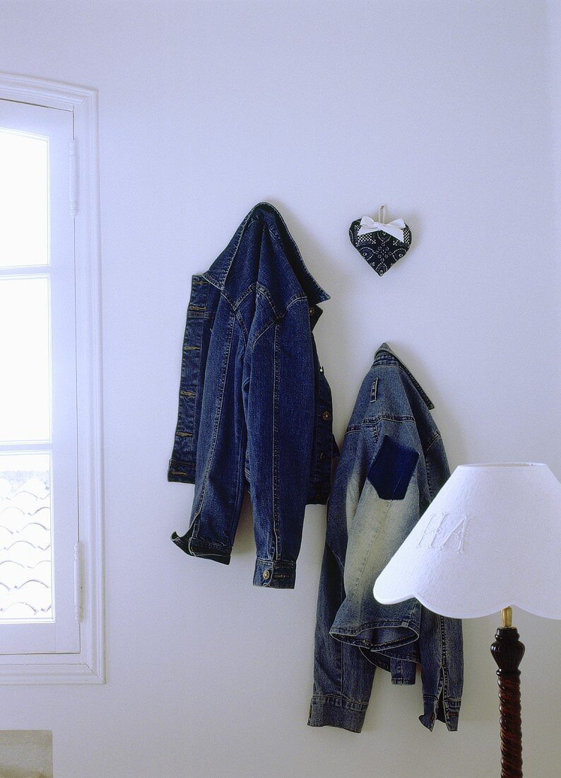 Blaue Jeansjacken hängen an einer weissen Wand