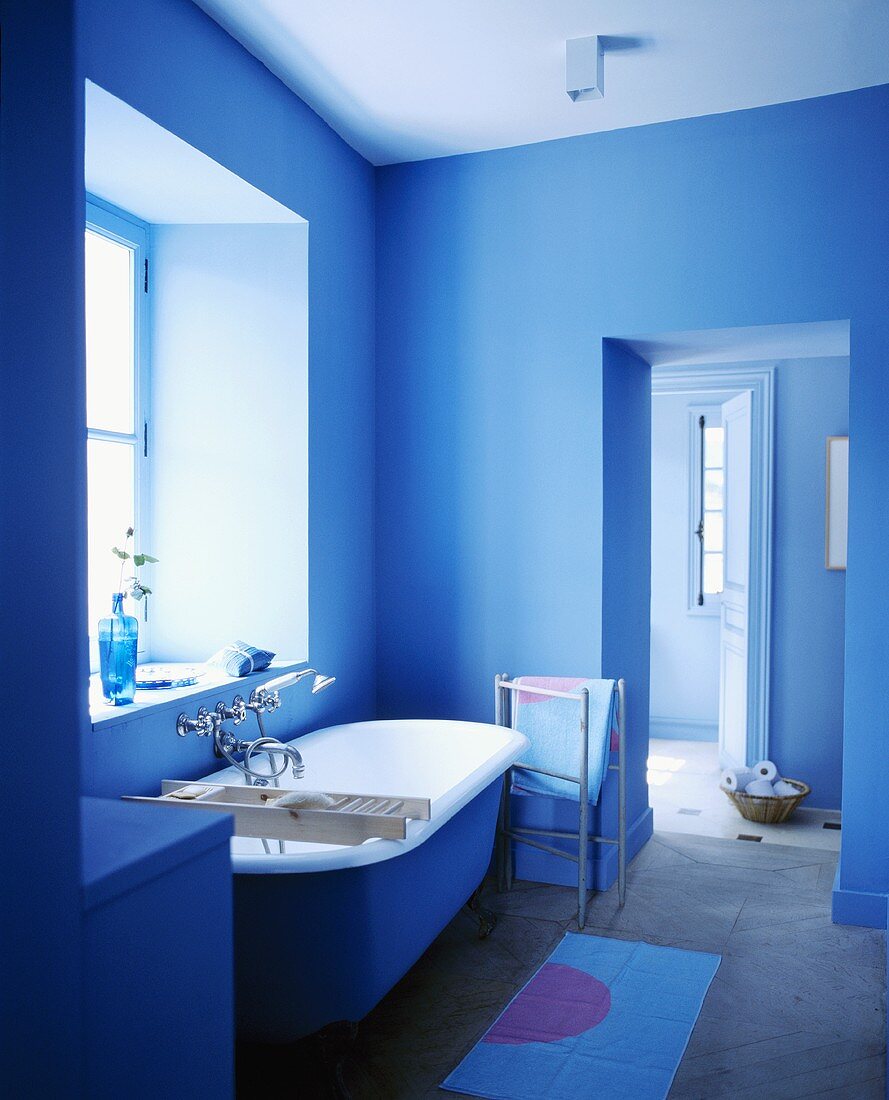 Frei stehende Badewanne vor dem Fenster in einem Badezimmer mit blauen Wänden