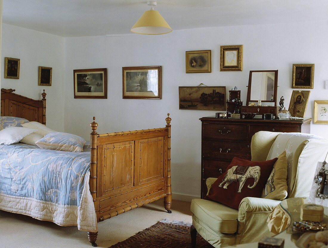 Traditionelles Schlafzimmer mit pastellblau-weisser Tagesdecke auf antikem Holzbett und Sammlung alter Bilder an der Wand