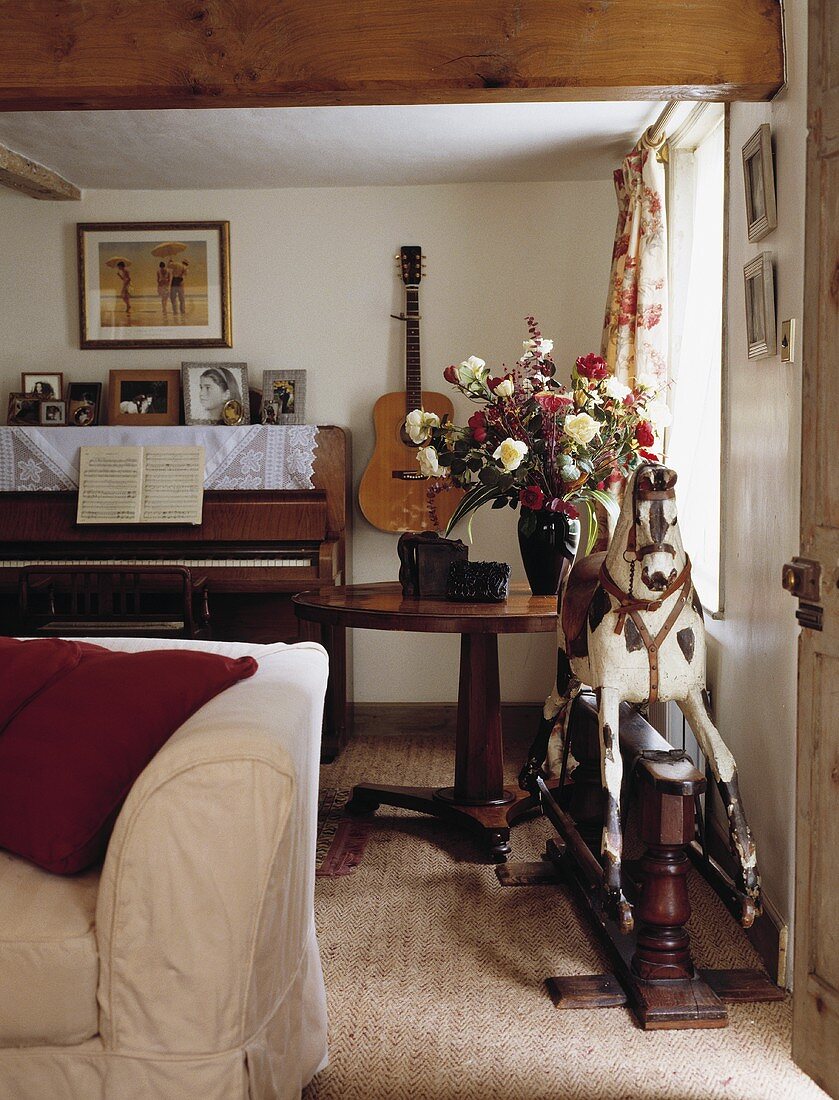 Antikes Schaukelpferd vor Klavier und Gitarre an der Wand in traditionellem Wohnzimmer
