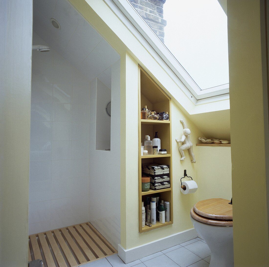 Grosses Dachflächenfenster über Toilettensitz in kleinem Dachgeschoss-Bad mit offener Dusche und eingebauten Regalen