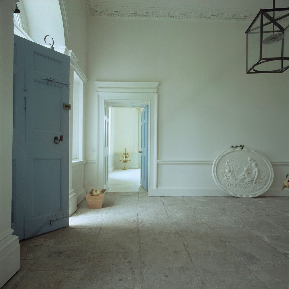 Ovales Gipsrelief auf hellem Natursteinboden in grossem georgianischen Saal mit pastellblauen Türen