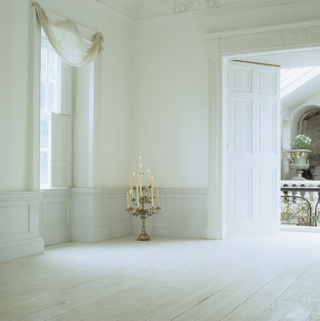 Weisser, unmöblierter Raum im Georgian Stil mit mehrstöckigem Leuchter mit brennenden Kerzen auf weißem Dielenboden