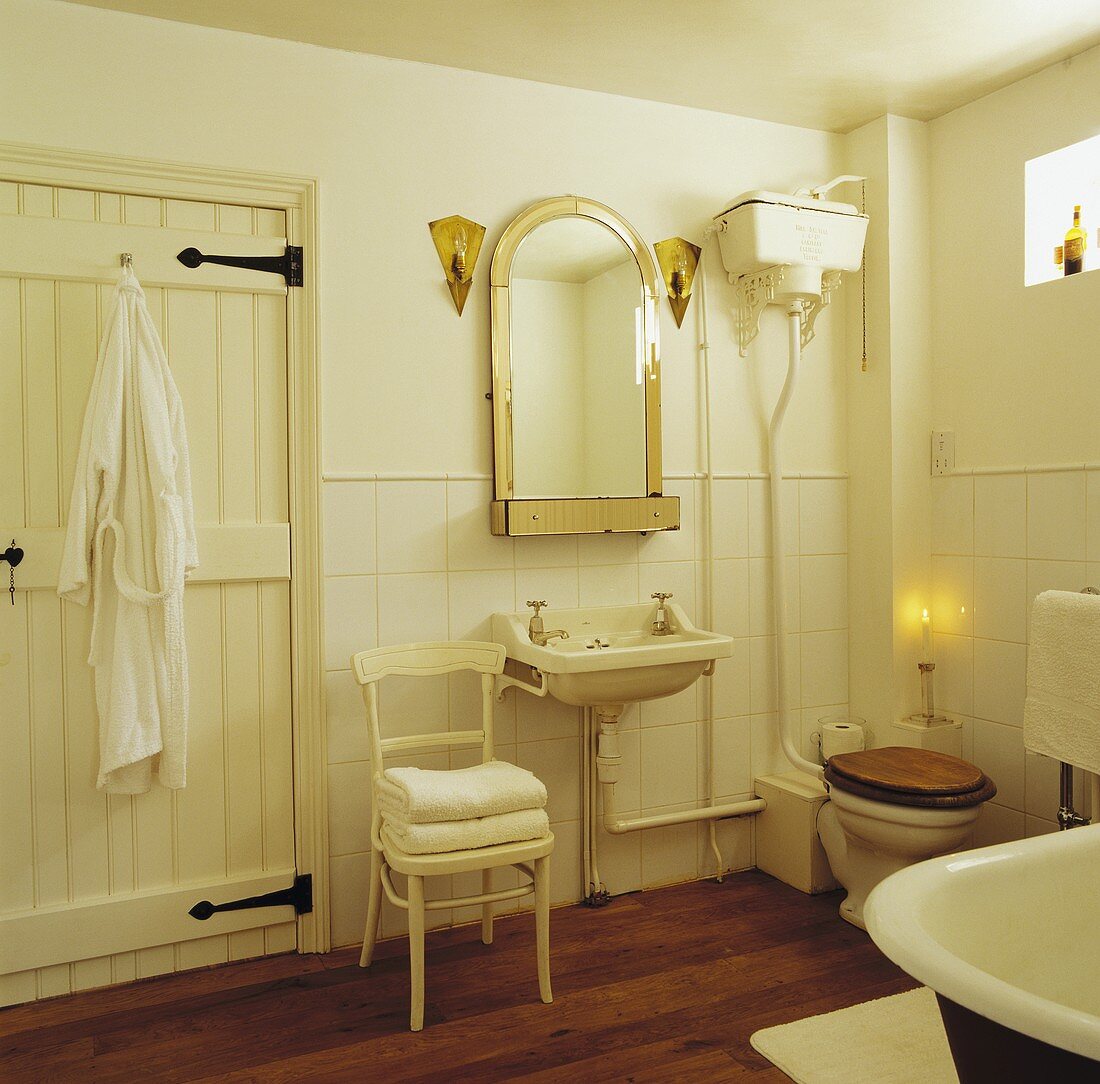 Cremefarbenes antikes Badezimmer mit honigfarbenen Lämpchen als Spiegelbeleuchtung und brennender Kerze neben WC
