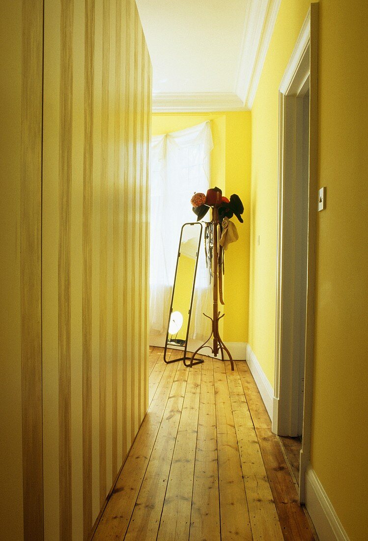 Dielenboden in schmalem, gelben Flur mit großem Spiegel und Hüten auf Garderobenständer