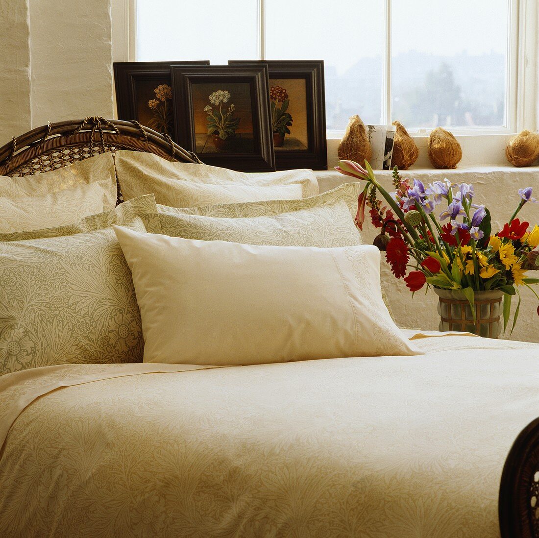 Antikes Bett mit cremefarbenen Kissen vor Bildern auf Fensterbank