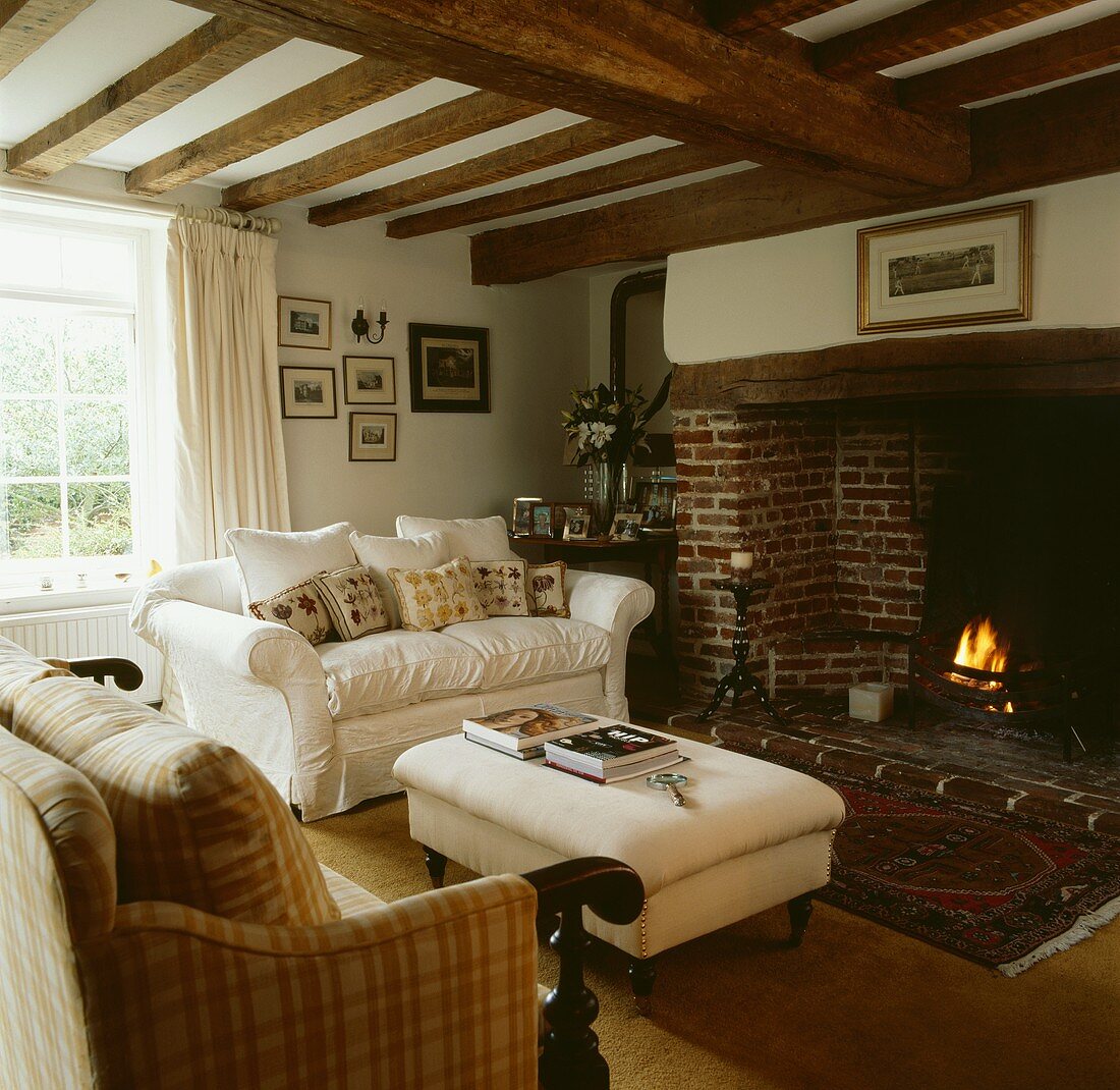 Polstersofas mit Kissen um einen brennenden Kamin in traditionellem Wohnzimmer mit Holzbalkendecke