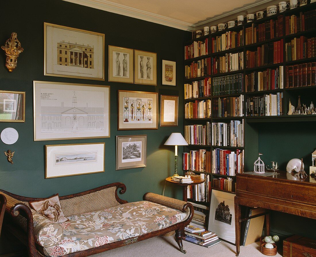 Eine antike Chaiselongue in einem dunkelgrünen Wohnzimmer mit Bücherwand auf der einen Seite