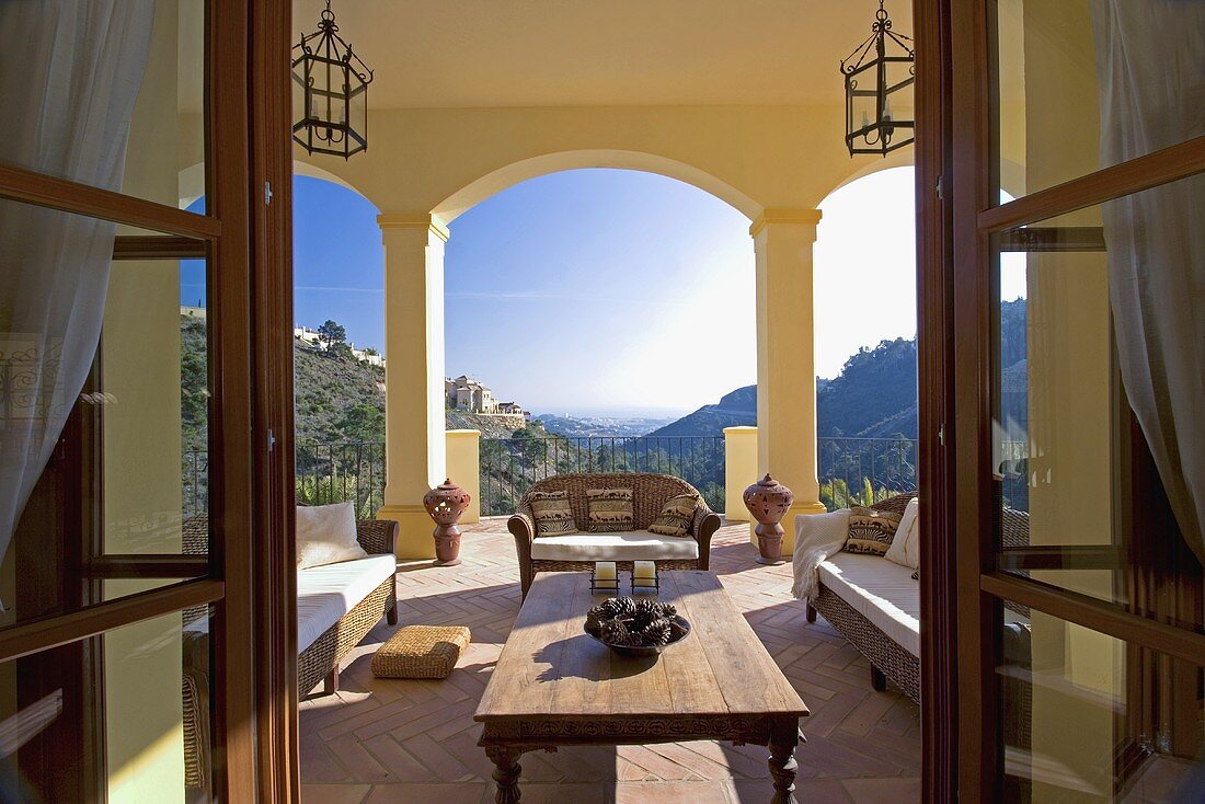 Sofas und ein Holztisch auf der Veranda der spanischen Villa mit Blick auf die Berge