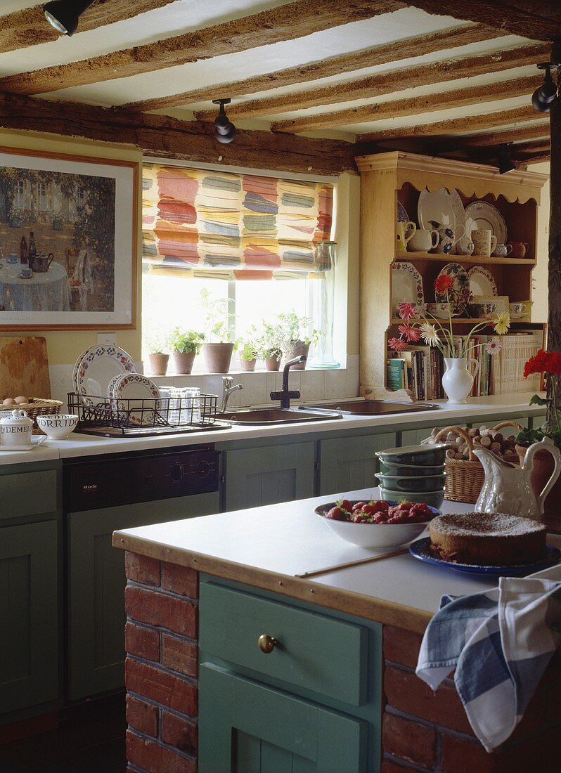 Eine ländliche Küche mit Kücheninsel und buntem Raffrollo über dem Spülbecken