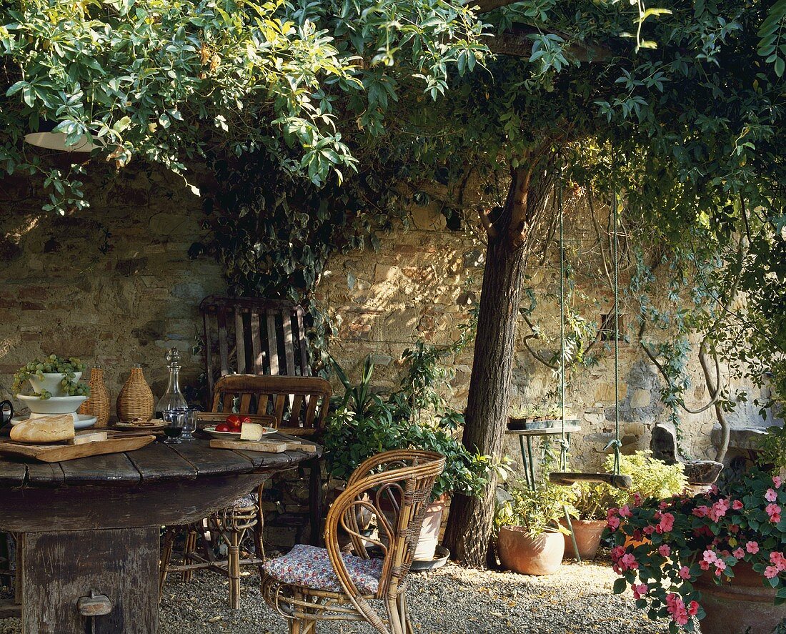 Rustikaler Holztisch unter dem Baum in einem ummauerten toskanischen Garten im Sommer