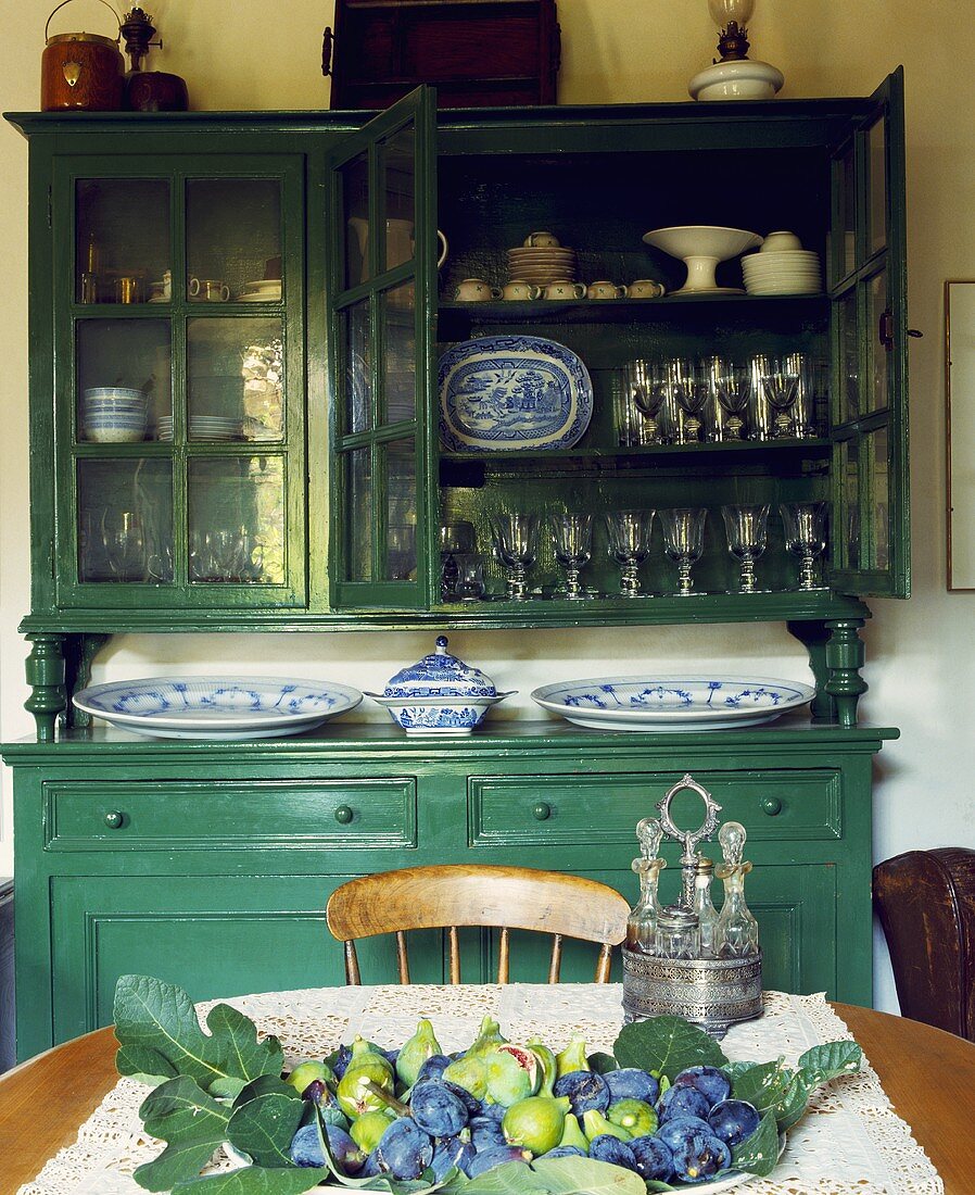Grosse grüne Anrichte mit blau-weißem Geschirr in einem ländlichen Esszimmer, auf dem Tisch eine Schale mit frischen Feigen und Weintrauben