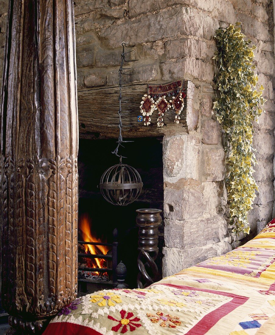 Patchwork-Tagesdecke auf dem Bett mit geschnitzten Holzpfosten im Landhausstil neben dem Naturstein-Kamin