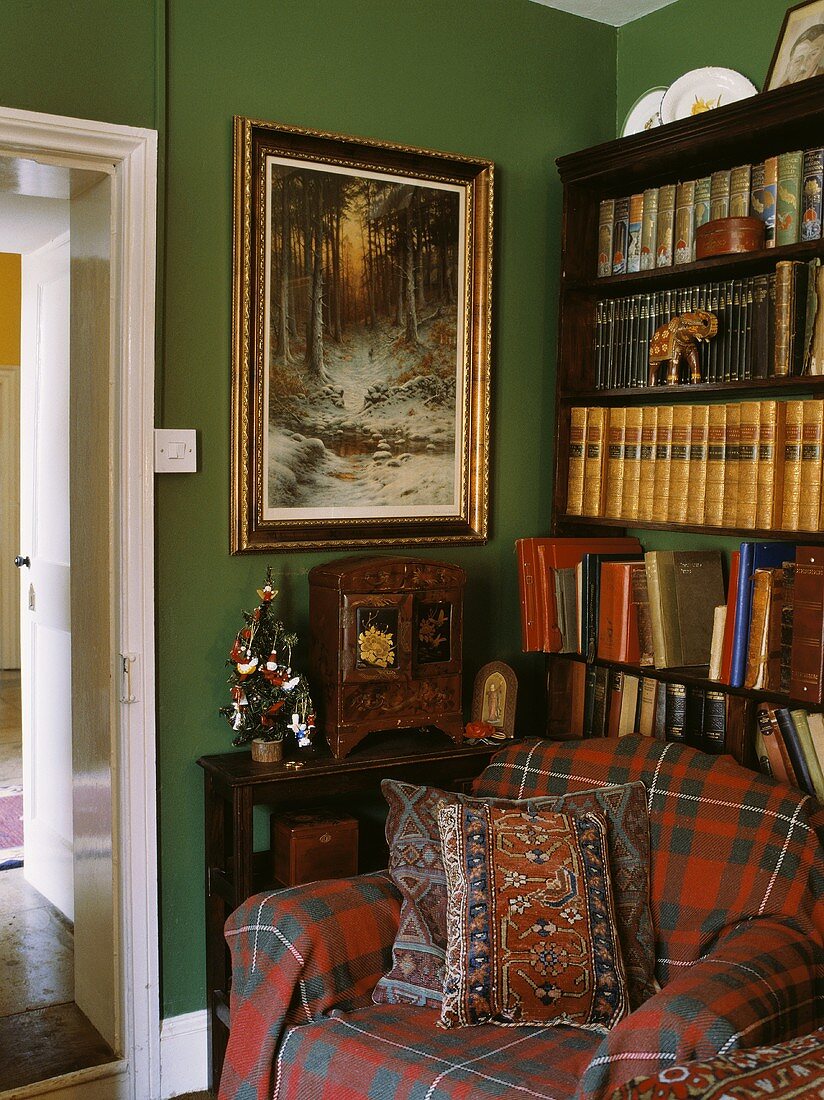 Ein Sessel mit karierter Decke vor dem Bücherregal in einem Wohnzimmer mit grüner Wand