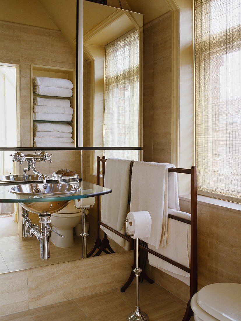 Glas und Edelstahl Becken an der Spiegelwand im modernen Bad mit weißen Handtüchern auf dem hölzernen Handtuchhalter