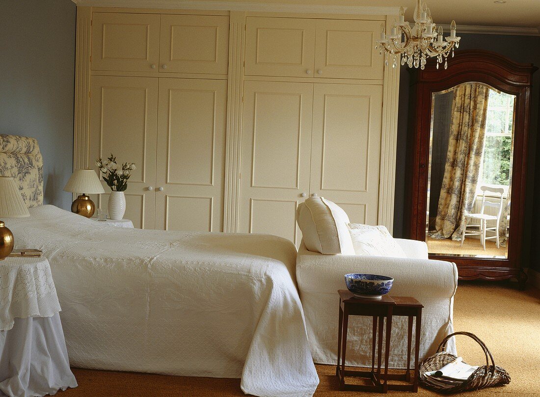Ein Bett mit weisser Bettwäsche, ein weisses Sofa, ein weisser Einbauschrank und ein antiker Spiegel in einem Schlafzimmer mit blauen Wänden