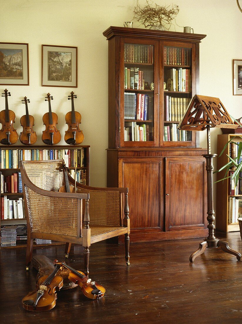 Antikes Bücherregal und kolonialer Rohrstuhl im Musikzimmer mit Holzfußboden und einer Sammlung von Geigen