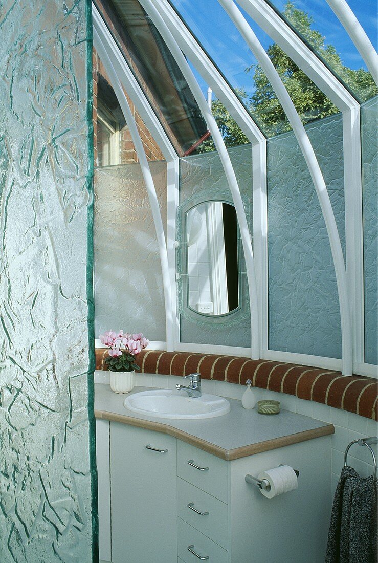 Grob bearbeitete Glaswände sorgen für Sichtschutz und statten das moderne Bad, das mit einem weißen Waschbecken und weißen Unterschränken eingerichtet ist, mit ausreichend Tageslicht aus