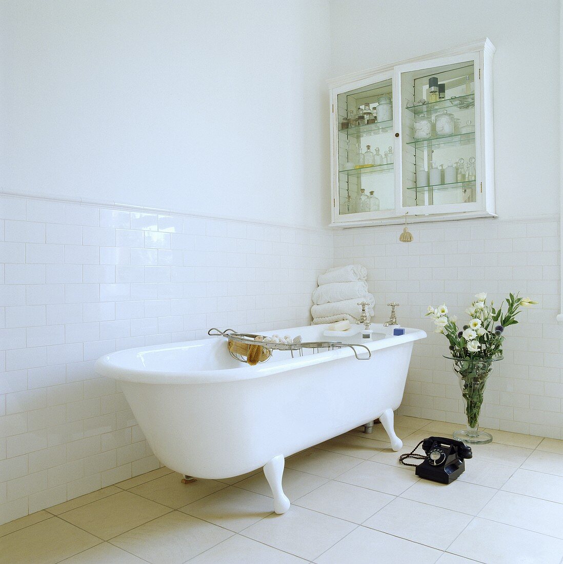 Eine freistehende Badewanne mit Klauenfüßen und ein altes Telefon stehen in der einen Ecke des modernen und weißen Badezimmers