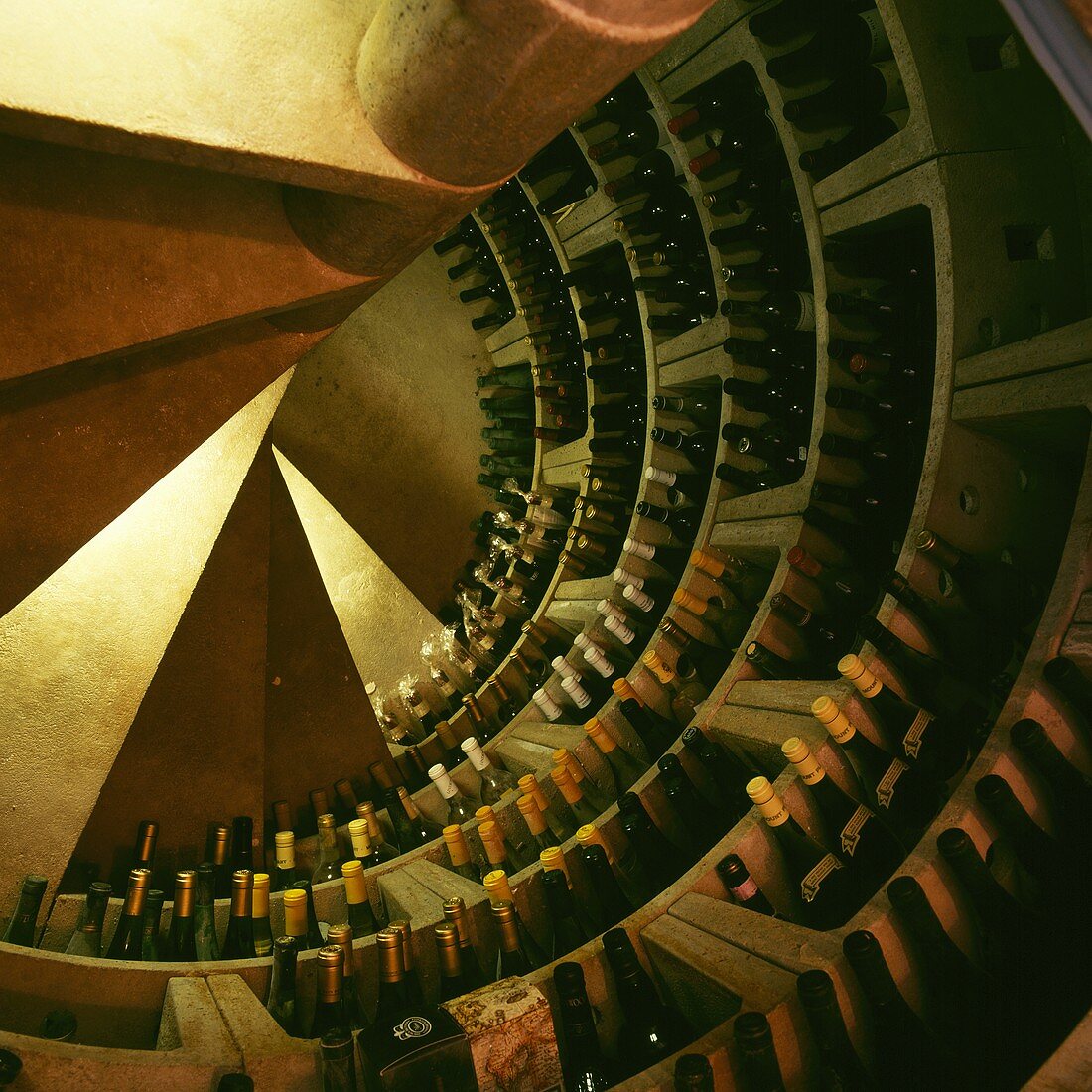 Luftaufnahme einer Wendeltreppe, die zu einem Kellerraum mit kreisförmigen Regalen für Weine führt