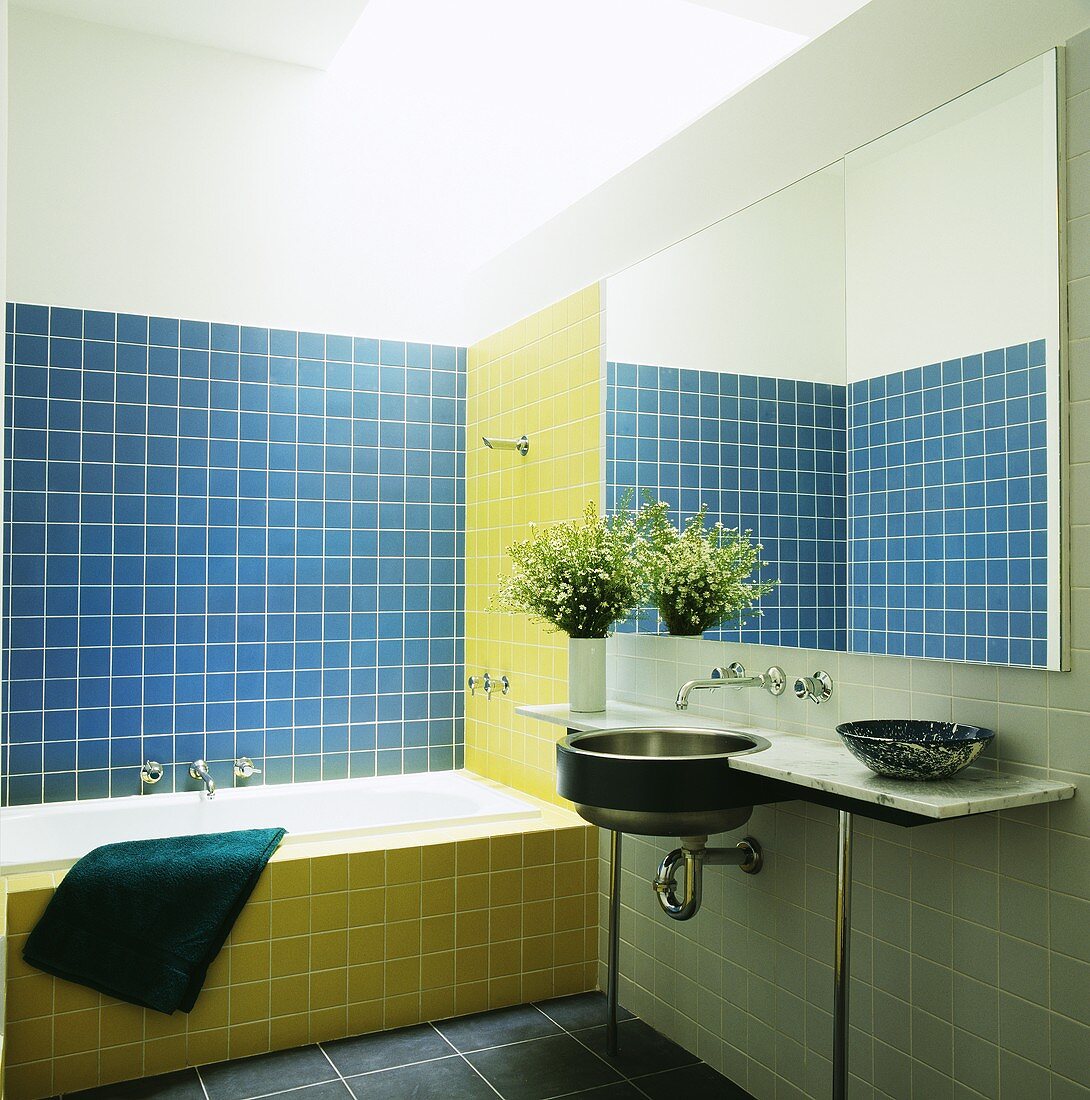 Ein Badezimmer mit blau-gelben Wandfliesen und ein Edelstahlwaschbecken, das unter einen Spiegel in einer Marmorplatte eingebaut ist