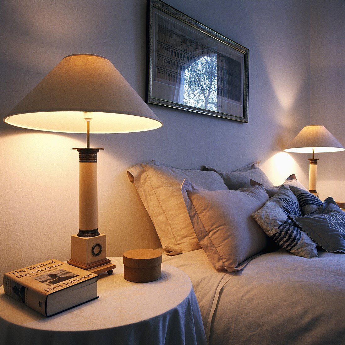 Zwei eingeschaltete Lampen, die an beiden Seiten eines Bettes mit hellgrauen Kissen und Bettwäsche stehen