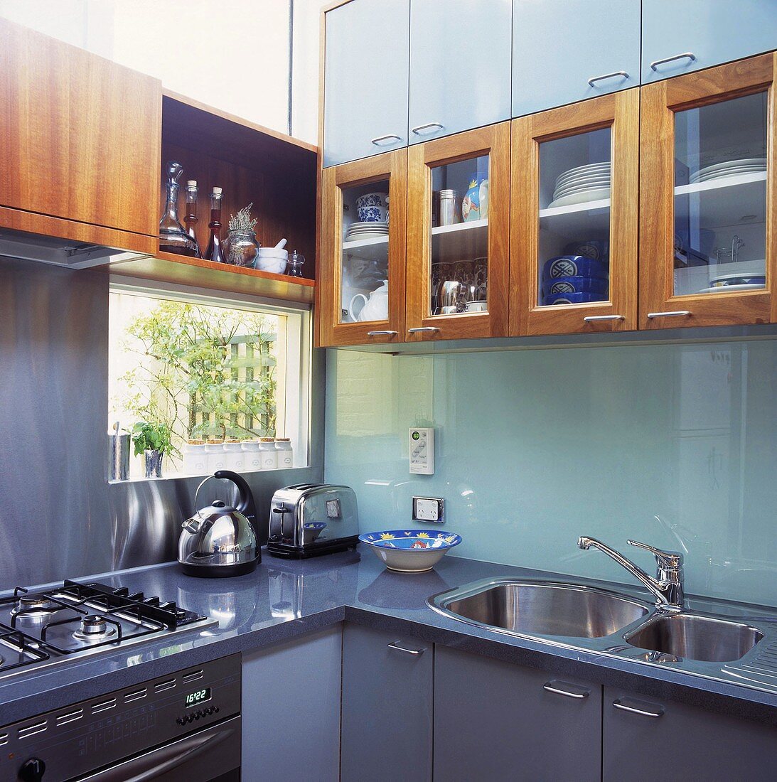In einer modernen Küche mit einem Edelstahl-Wasserkocher und einen Toaster sind Glas-Einbauschränke über einer Glas Rückwand angebracht worden